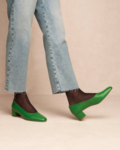 Model wearing Oya Culford heel in bright emerald green, low heel women's shoes for extended sizes, one shoe points upwards with heel on ground.